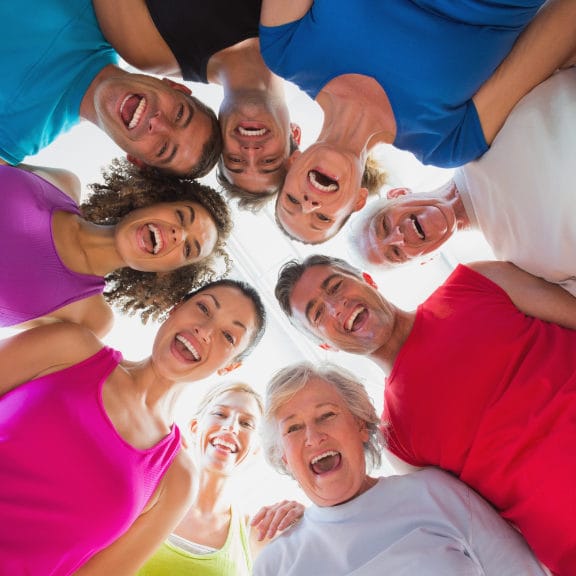 Group of people dressed in bright tshirts, standing in a circle and looking down at the camera